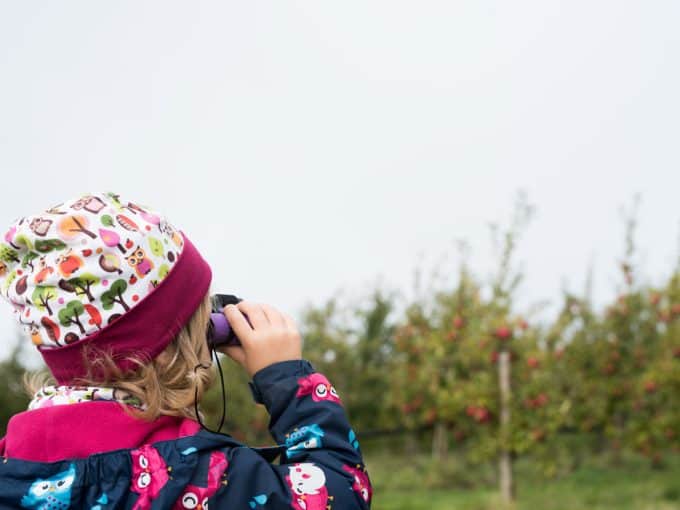 Ein kleines Mädchen schaut durch ihr Fernglas in die Natur. 