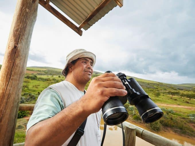 Ein Mann ist in der Natur und hält ein Fernglas in der Hand. 