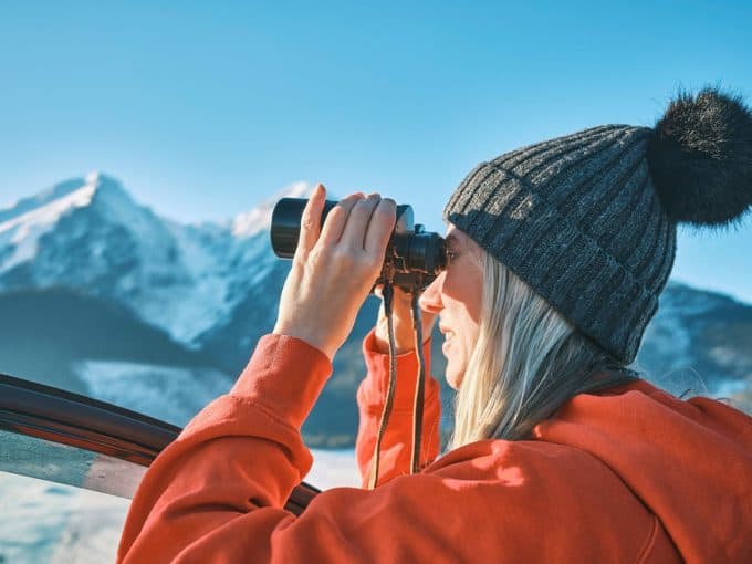 Eine Frau schaut mit einem Fernglas in die schneebedeckte Landschaft.