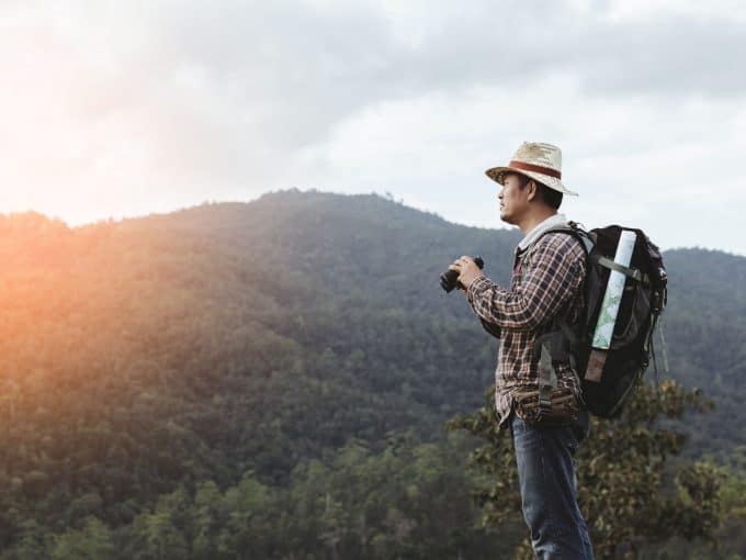 Ein Mann genießt die Aussicht auf einem Berg und hält ein Fernglas in der Hand.